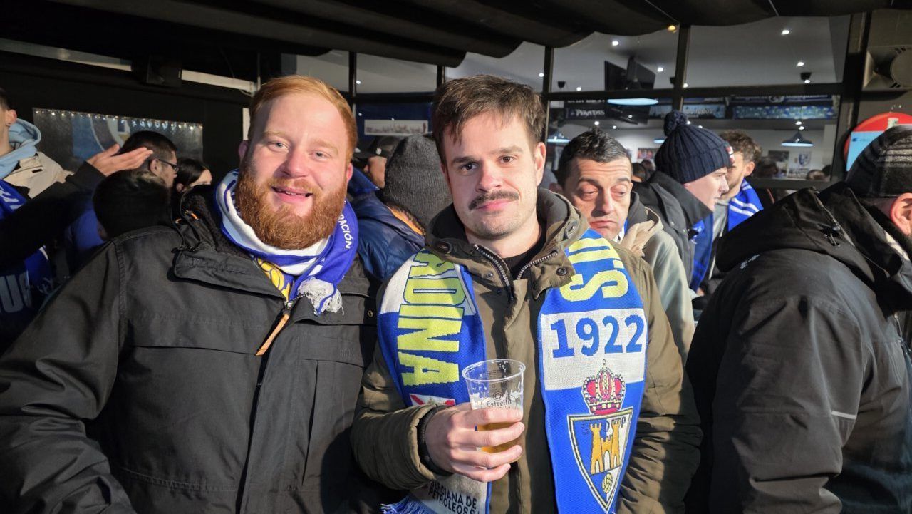 Dos aficionados sonrientes con bufandas en un evento deportivo