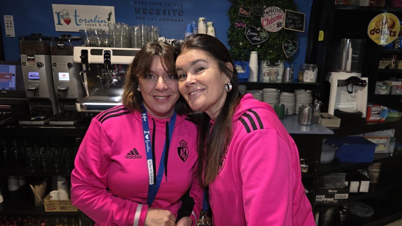 Dos mujeres sonriendo en un bar con ropa deportiva rosa