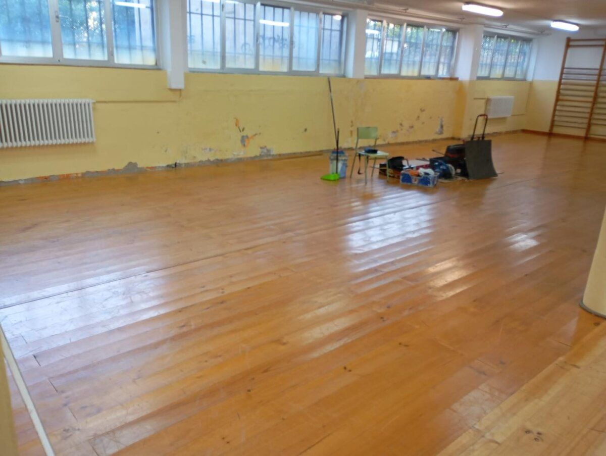 Interior del Colegio San Miguel con piso de madera y herramientas de limpieza