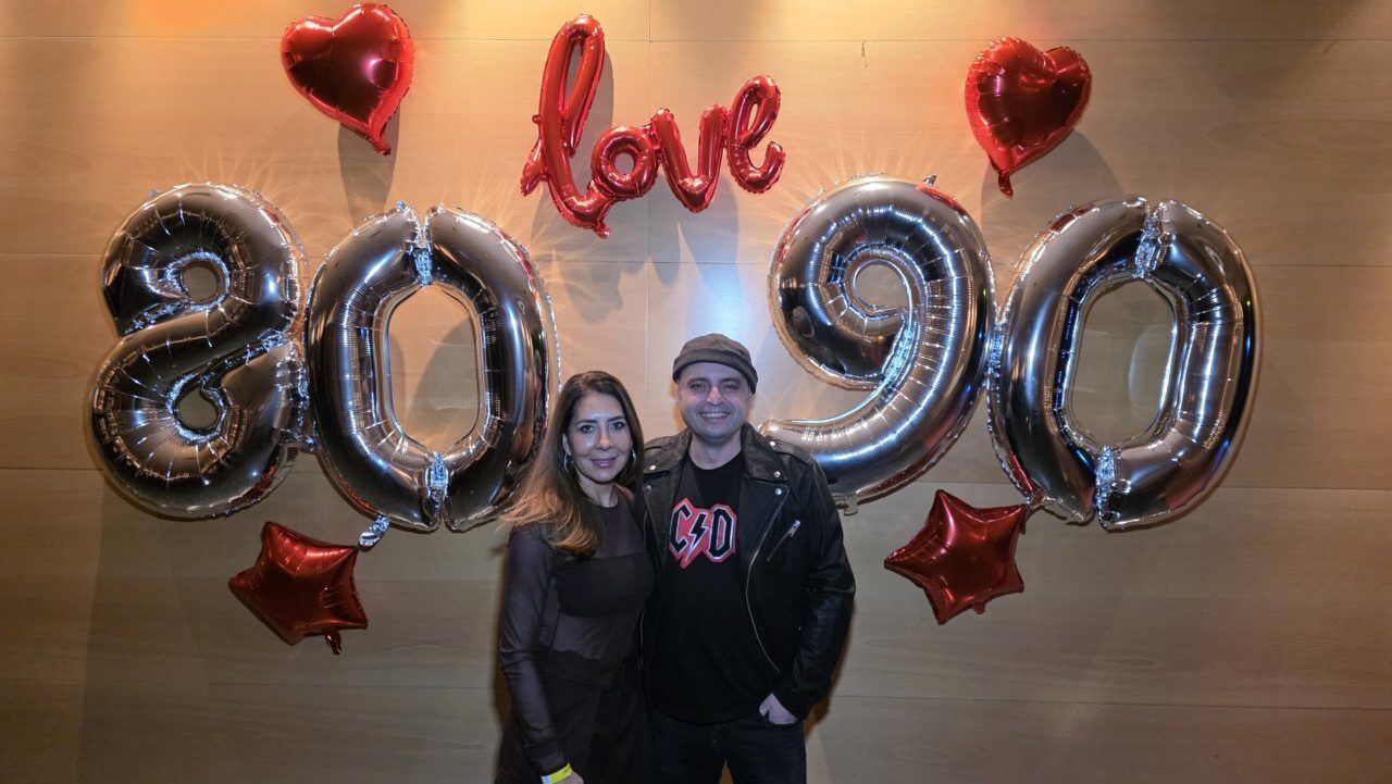 Pareja posando frente a globos de fiesta de los años 80 y 90