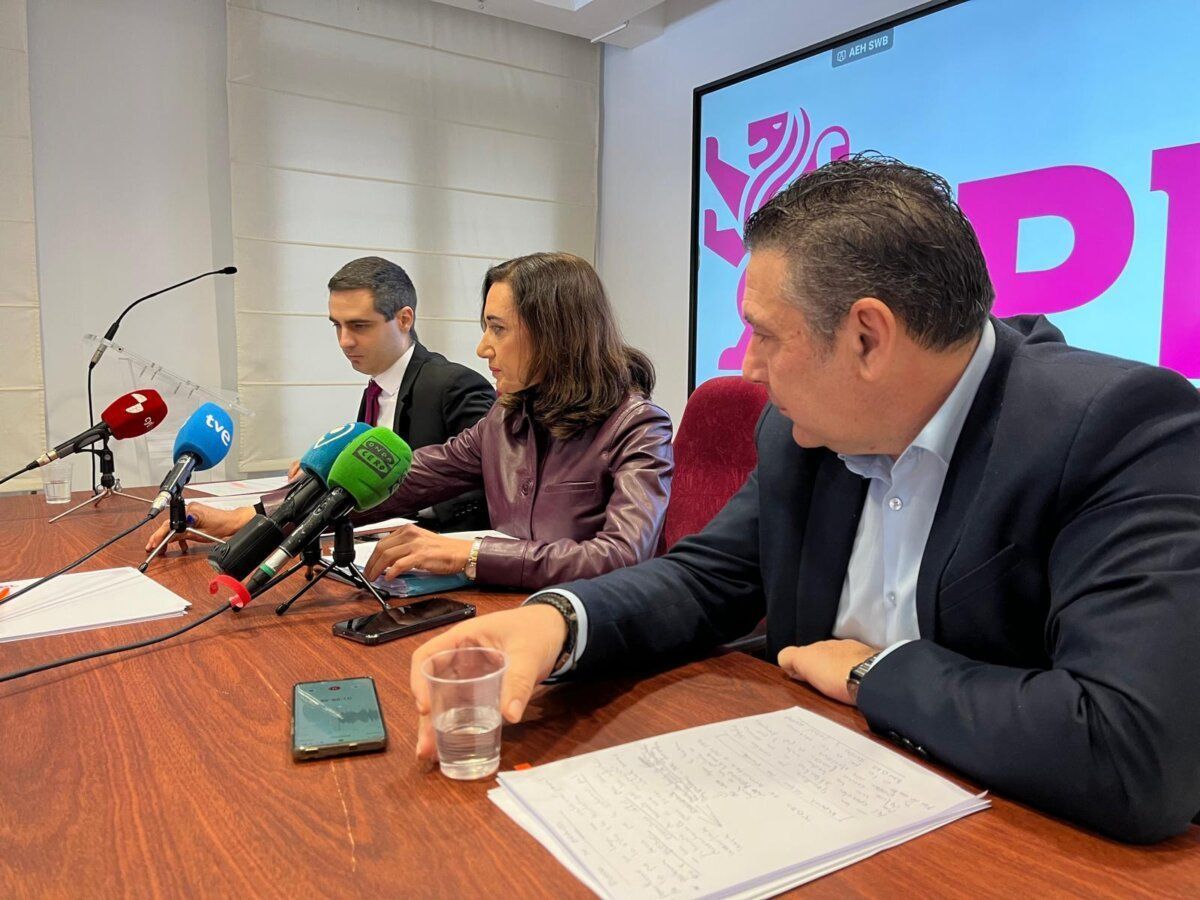Tres personas en una rueda de prensa con micrófonos y documentos