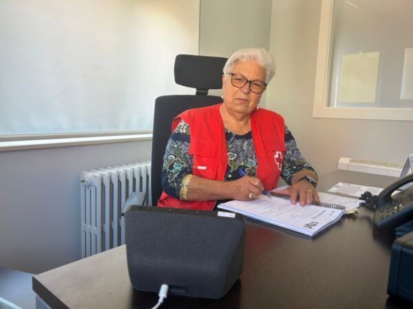 Mujer mayor con chaleco de Cruz Roja escribiendo en una oficina