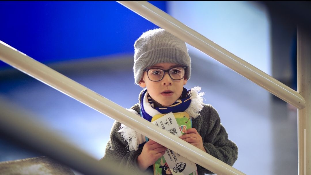 Niño con gorro y gafas sosteniendo entradas en un evento deportivo