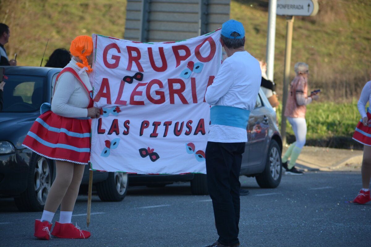 Participantes del desfile de carnaval en Cacabelos con un cartel colorido.