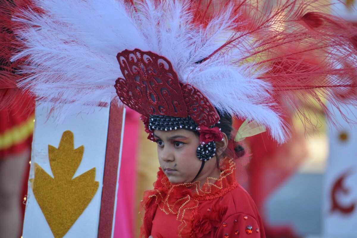 Niña con disfraz rojo y plumas en desfile de Carnaval en Cacabelos