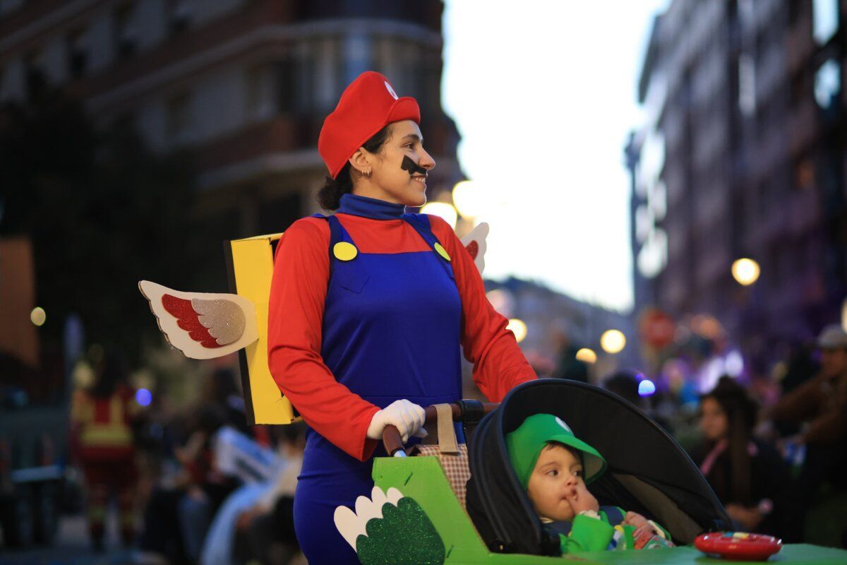 Mujer disfrazada de Mario con un niño en un carrito en el carnaval