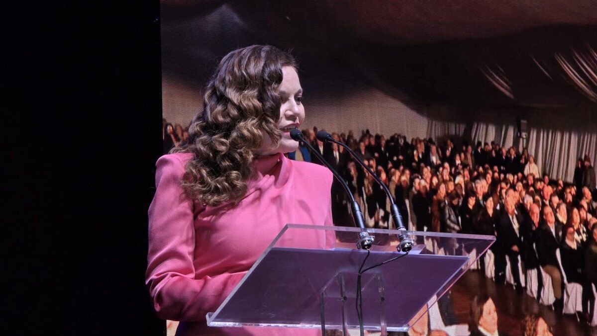 Mujer hablando en un evento con público al fondo