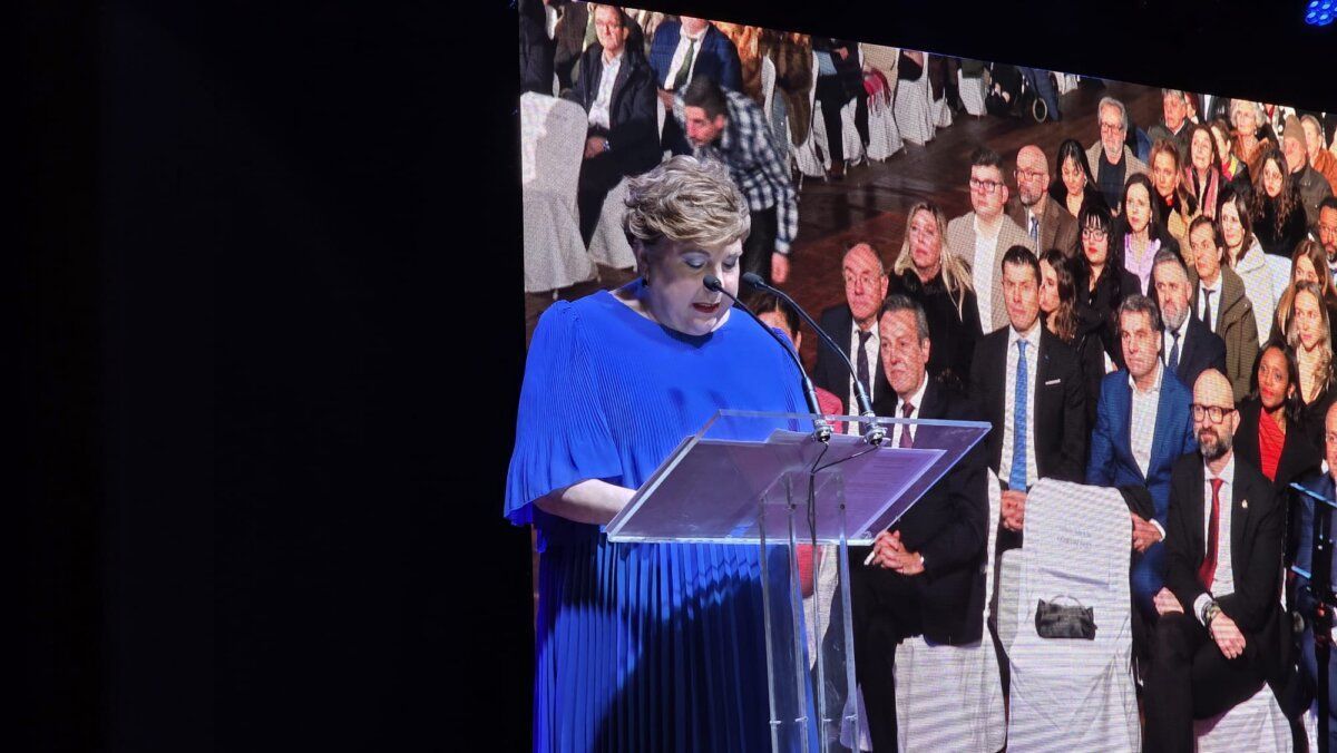 Mujer en vestido azul hablando en un evento con público al fondo
