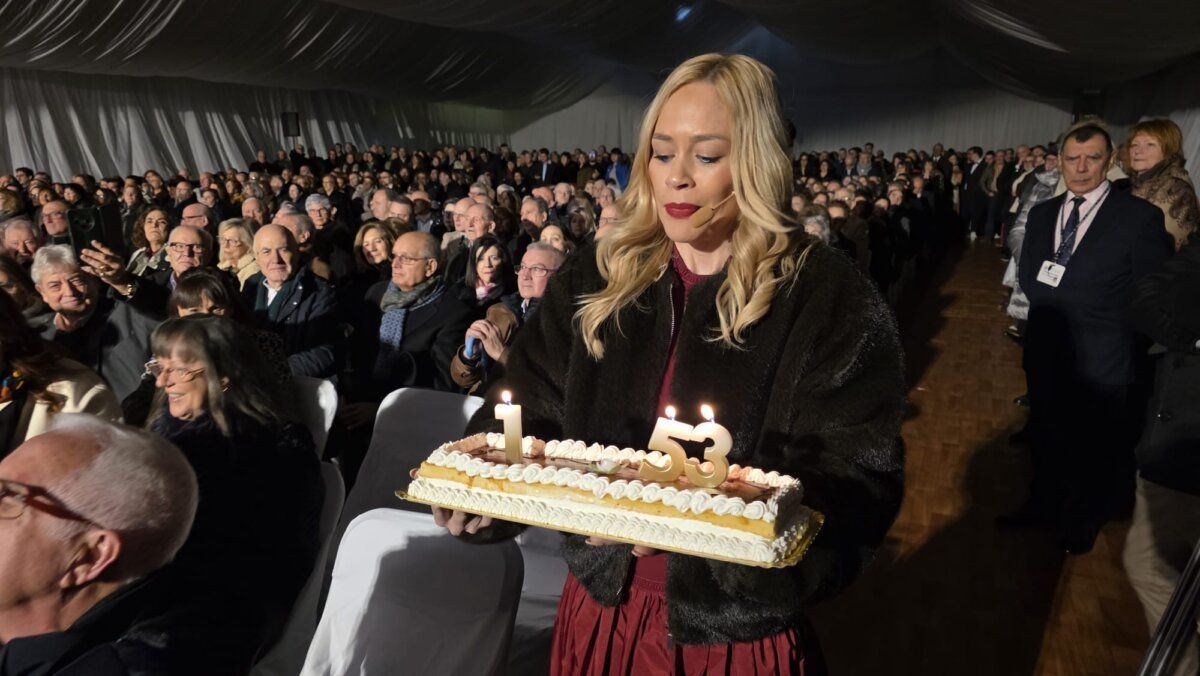 Mujer sosteniendo un pastel con velas en un evento multitudinario