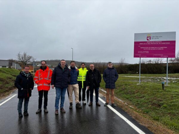 Grupo de personas en la carretera de acceso a Corcos con cartel de obras
