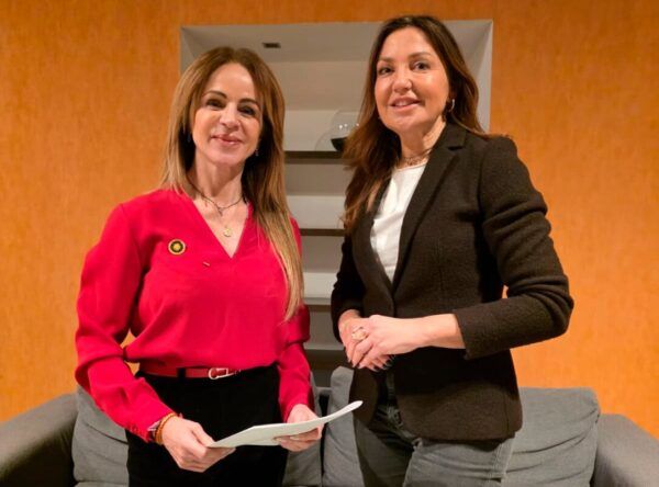 Dos mujeres posando en un ambiente interior con documentos en mano