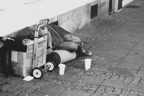 Persona en situación de calle en un entorno urbano con cartón y objetos personales.