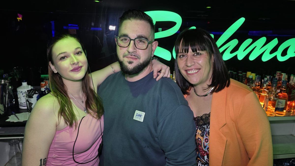 Tres personas posando en un bar con luces verdes de fondo