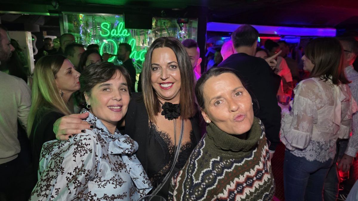 Tres mujeres sonriendo en una fiesta con luces de colores