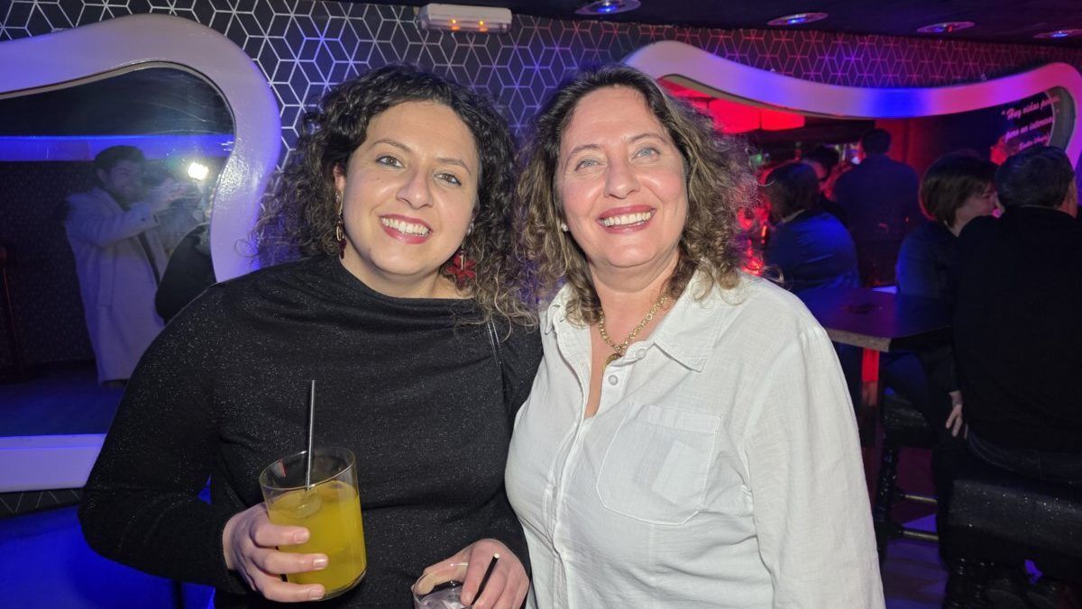 Dos mujeres sonriendo en un bar con luces de colores