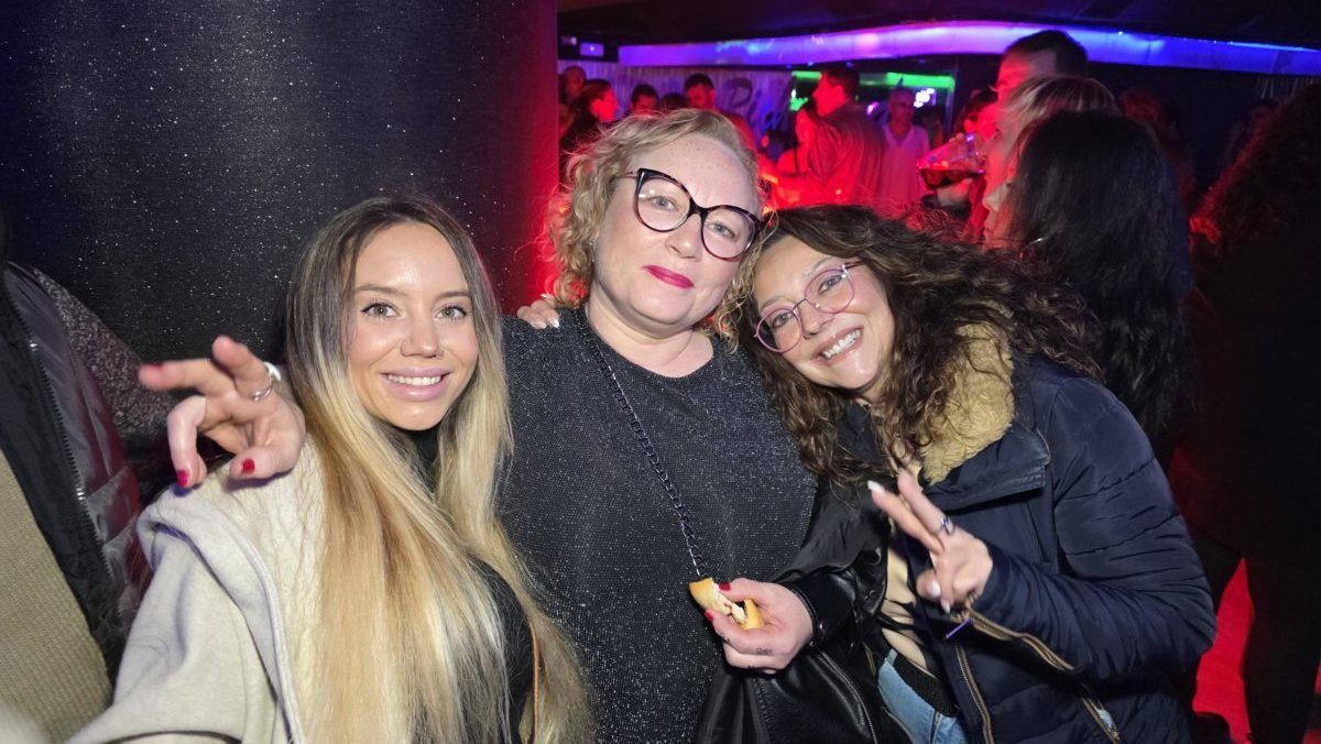 Tres mujeres sonrientes en una fiesta con luces de colores