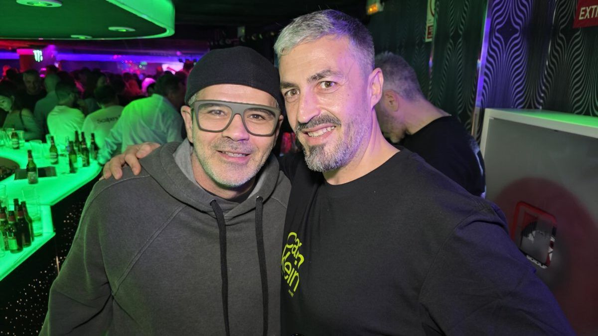 Dos hombres sonriendo en un bar con luces de colores