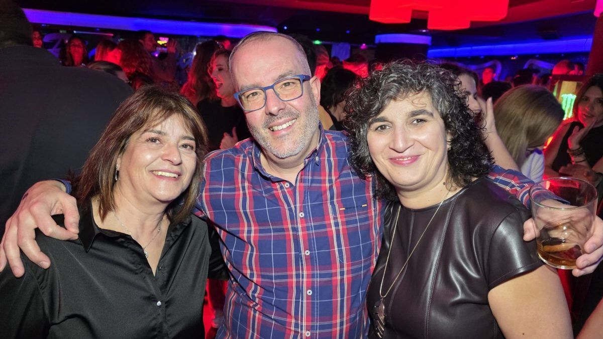 Tres personas sonriendo en una fiesta con luces de colores