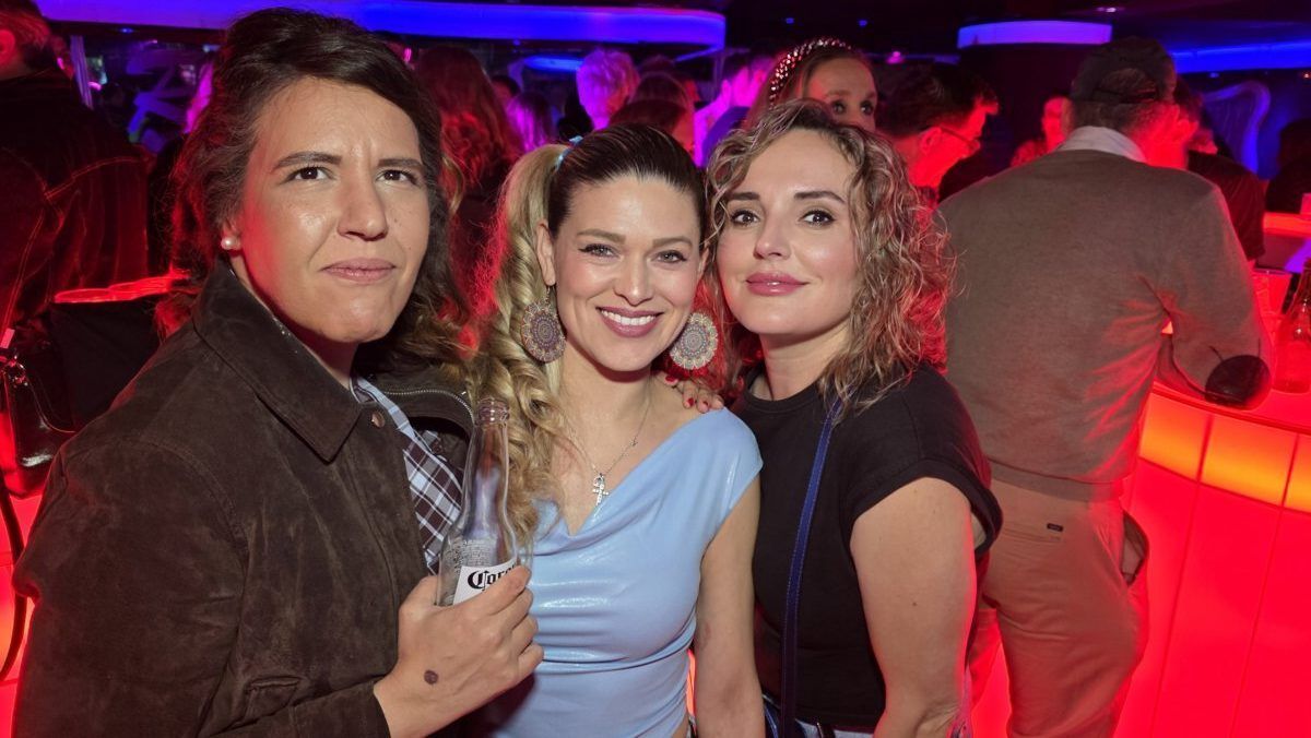 Tres mujeres sonriendo en una fiesta con luces de colores