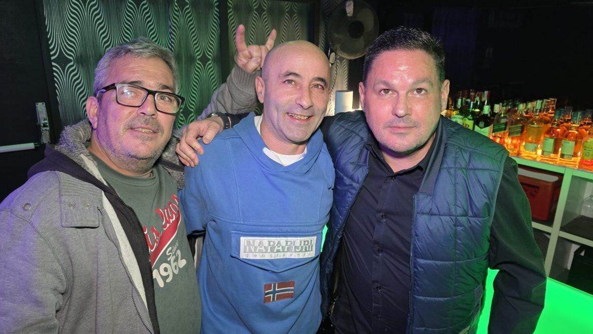 Tres hombres posando en una fiesta con fondo de bar iluminado