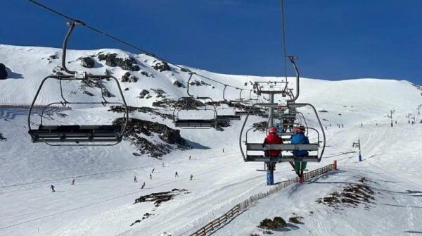 Esquiadores en un telesilla en San Isidro con nieve y montañas