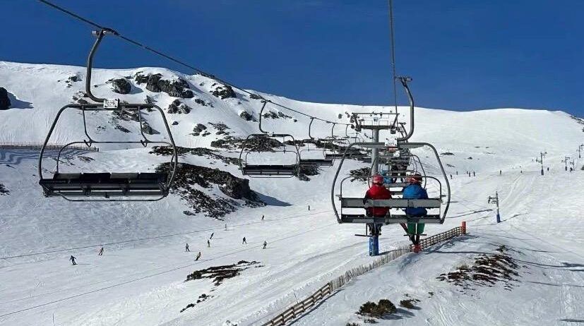 Esquiadores en un telesilla en San Isidro con nieve y montañas