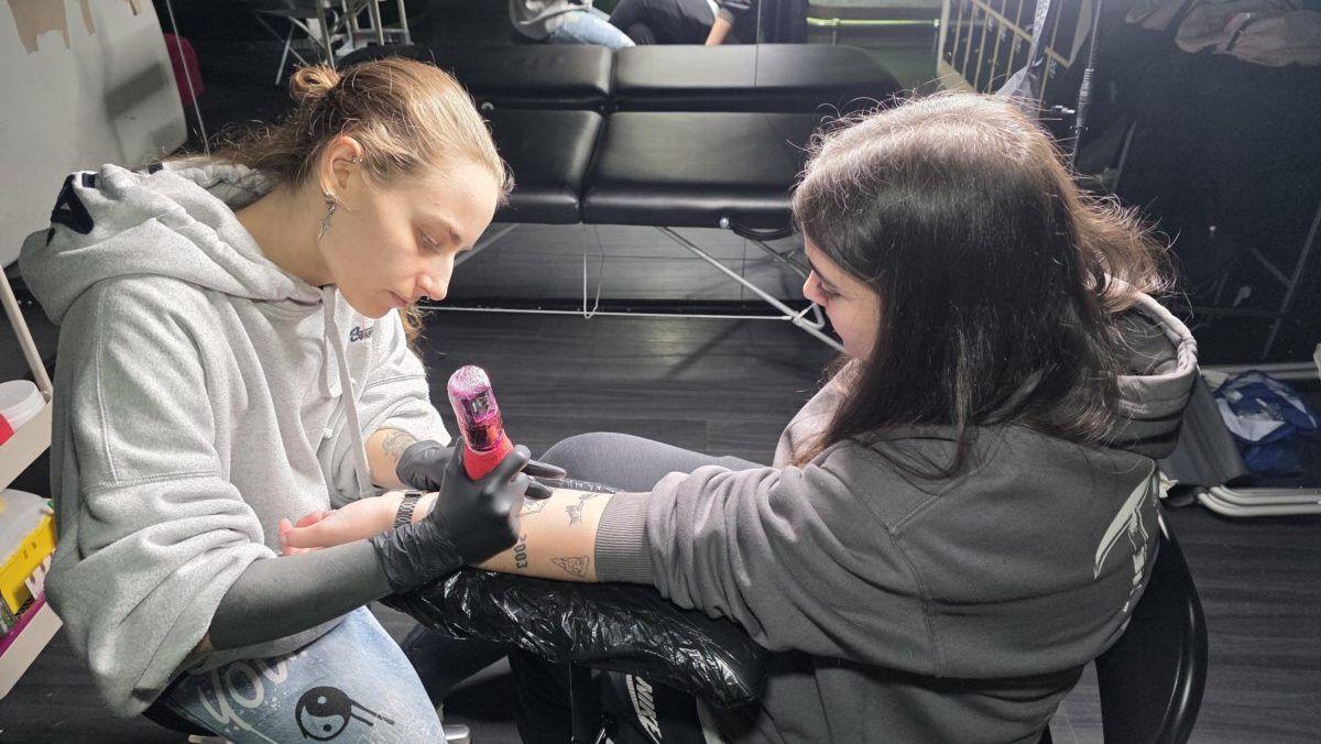 Artista de tatuajes trabajando en el brazo de una cliente en un estudio