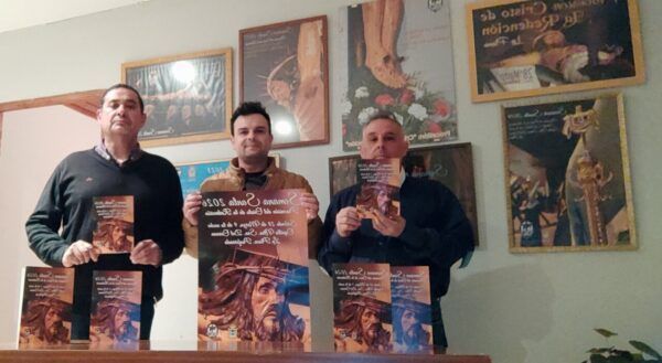 Tres hombres sosteniendo carteles de la Hermandad en un evento
