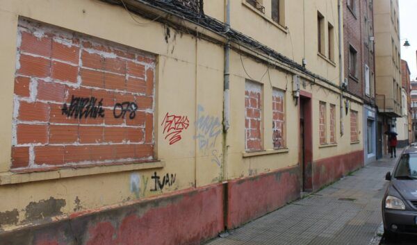 Vista de un barrio vulnerable en León con grafitis y ventanas cerradas.