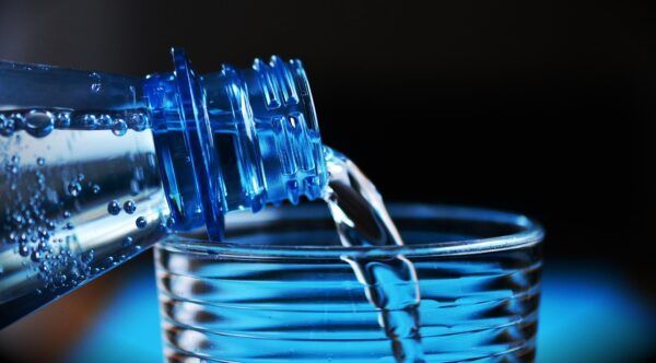 Botella de agua vertiendo en un vaso transparente