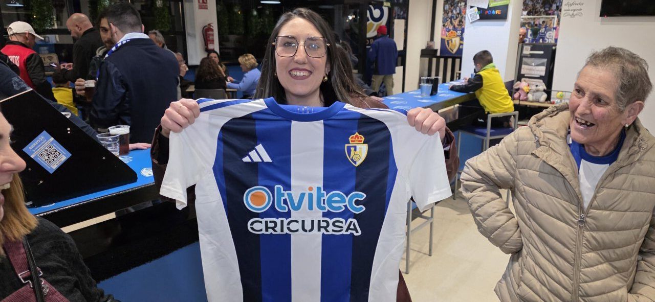 Mujer sonriente sosteniendo camiseta del equipo Ponfe en bar