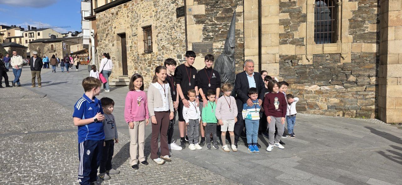 Grupo de niños y adultos posando junto a una escultura del Lambrión Chupacandiles en Ponferrada