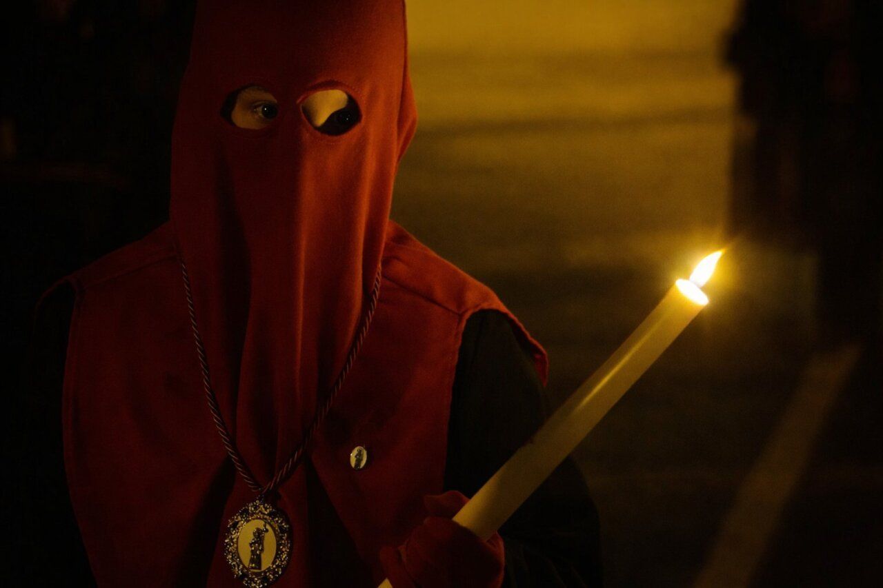 Niño con capirote rojo sosteniendo una vela en la procesión