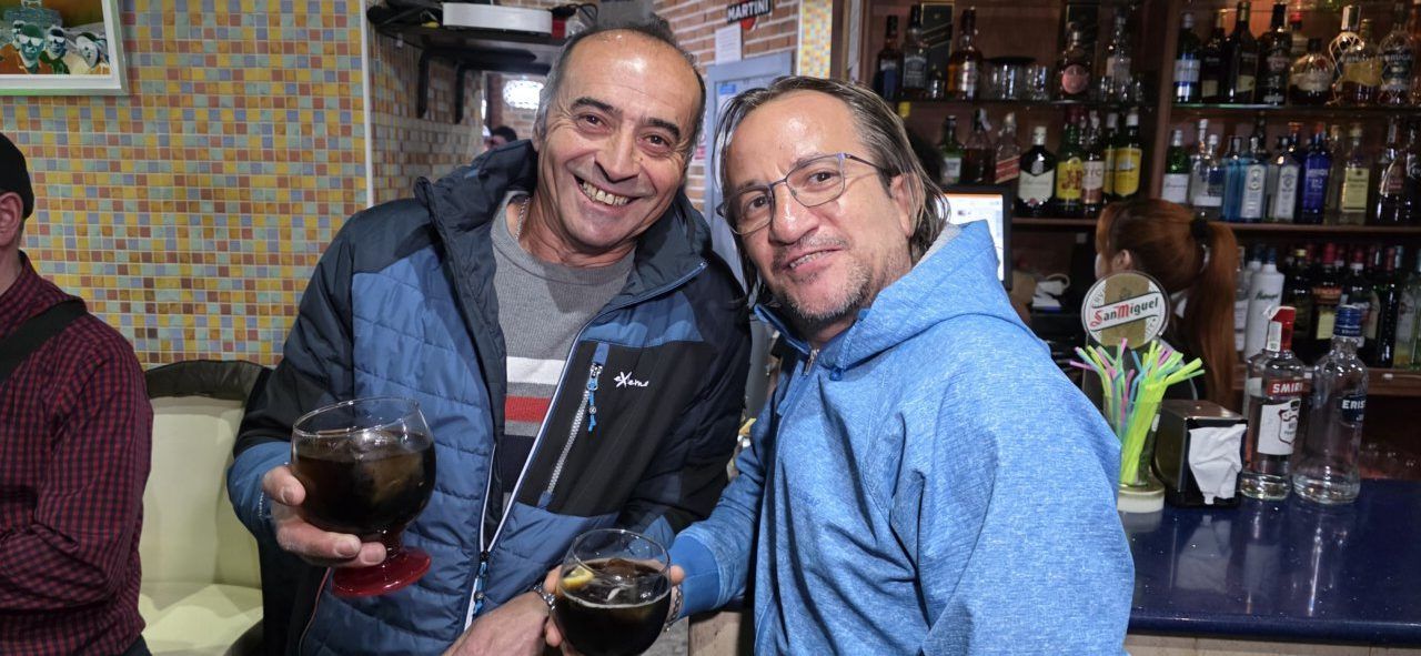 Dos hombres sonrientes sosteniendo vasos en un bar