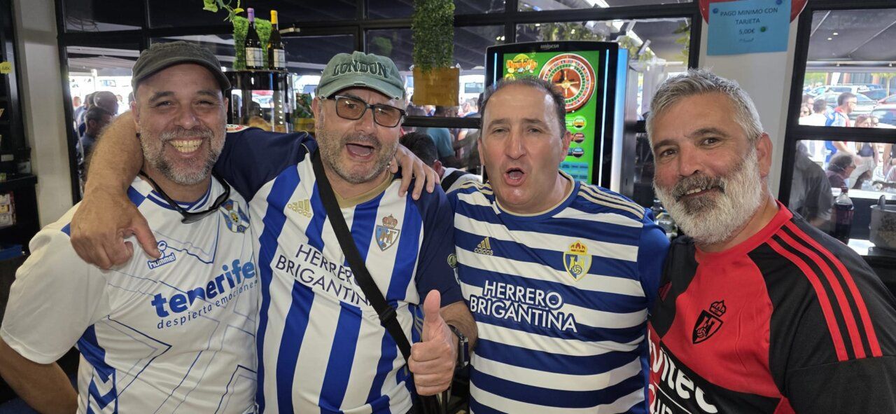 Cuatro aficionados celebrando en un bar, vistiendo camisetas de fútbol.