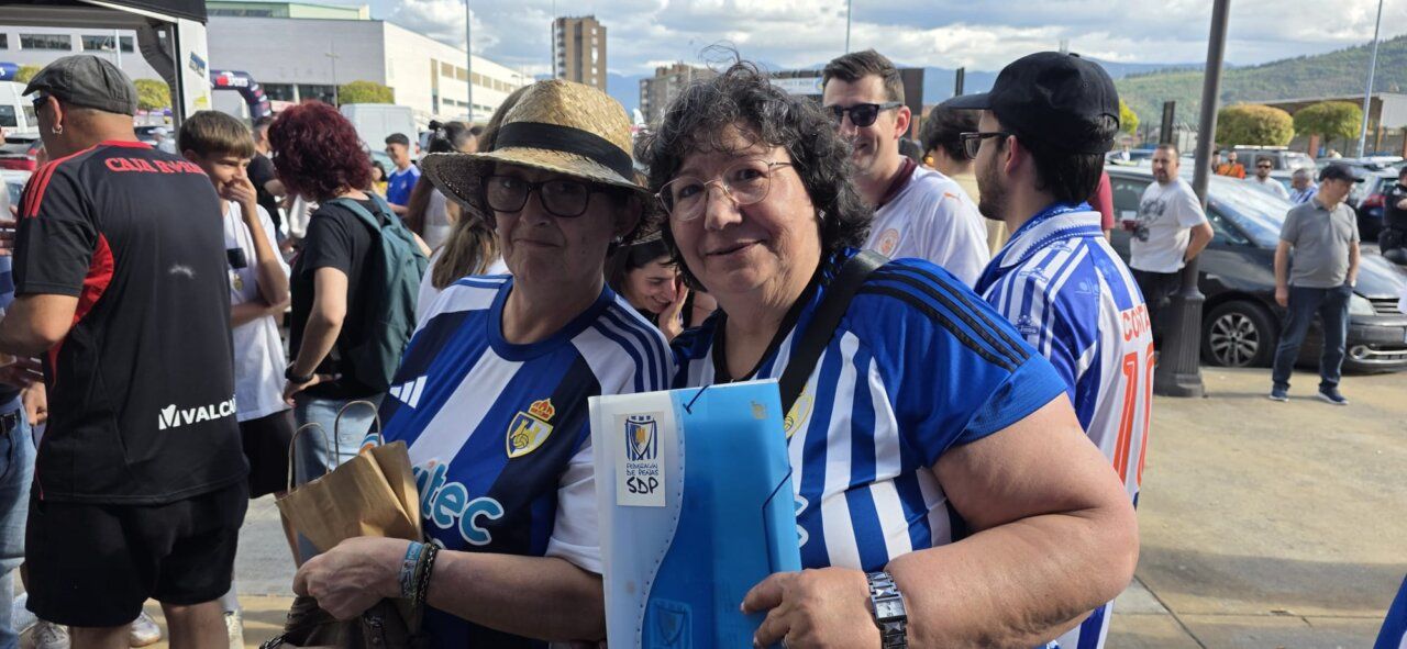 Dos mujeres sonriendo con camisetas de fútbol en un evento deportivo.