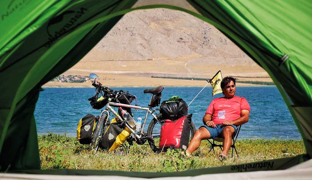 Néstor Yuguero sentado junto a su bicicleta en un paisaje natural