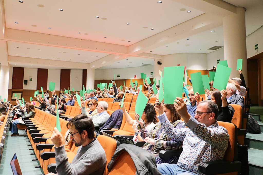 Asamblea del Claustro universitario con participantes levantando carteles verdes