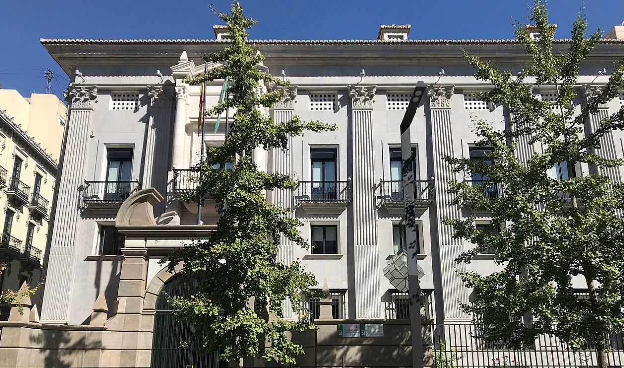 Edificio institucional con árboles en primer plano y cielo azul