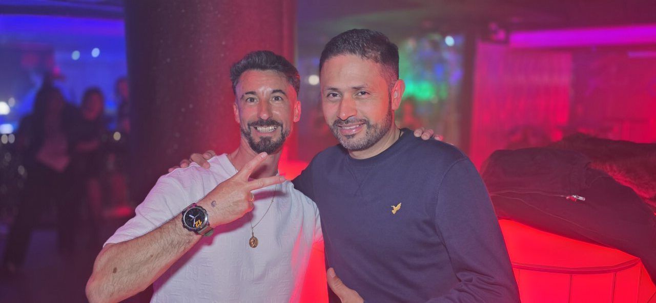 Dos hombres sonriendo en una fiesta con luces de colores