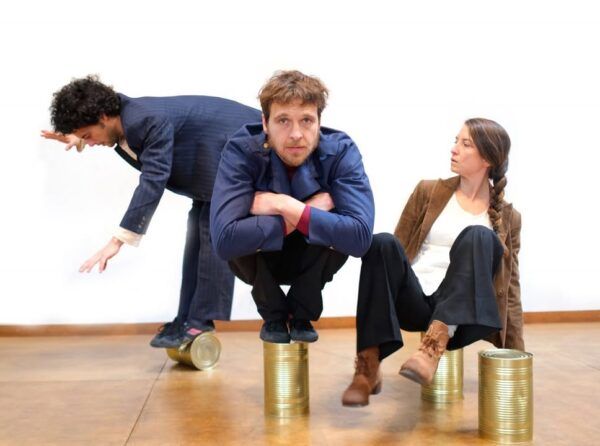 Tres artistas de circo realizando acrobacias sobre latas