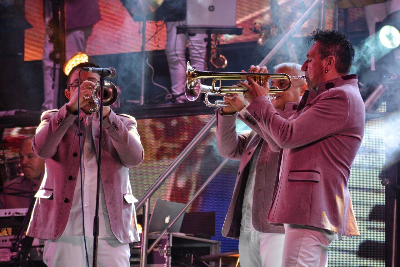 Músicos de la Orquesta Los Satélites tocando trompetas en un concierto