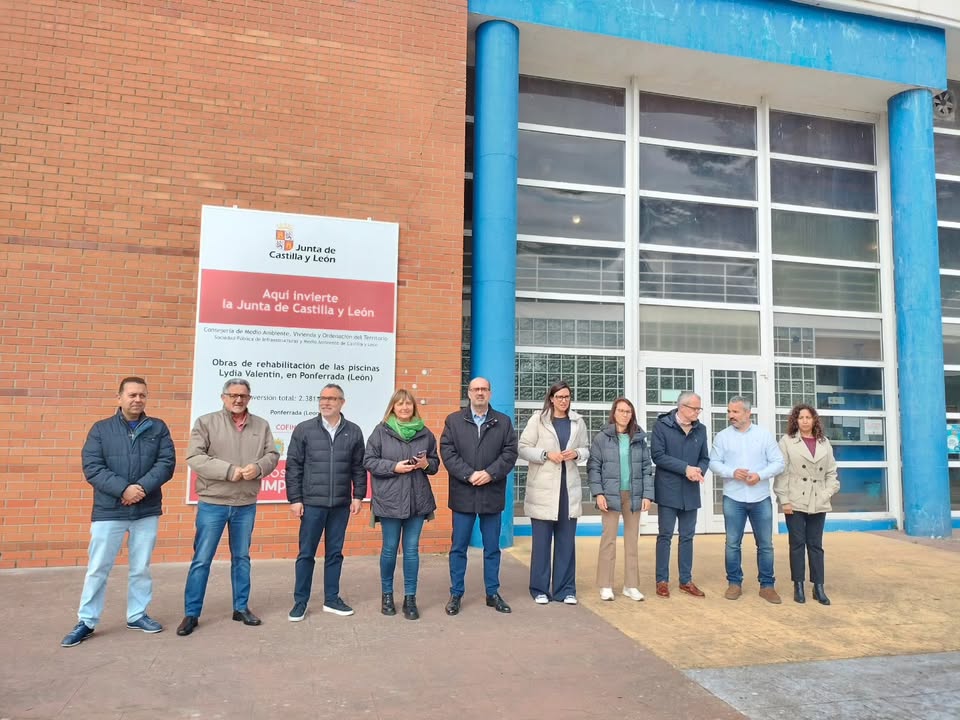 Grupo de personas frente a un cartel sobre la rehabilitación de piscinas en Ponferrada