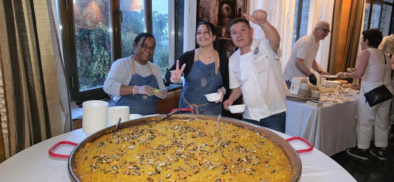 Tres personas sonrientes junto a una gran paella en un evento