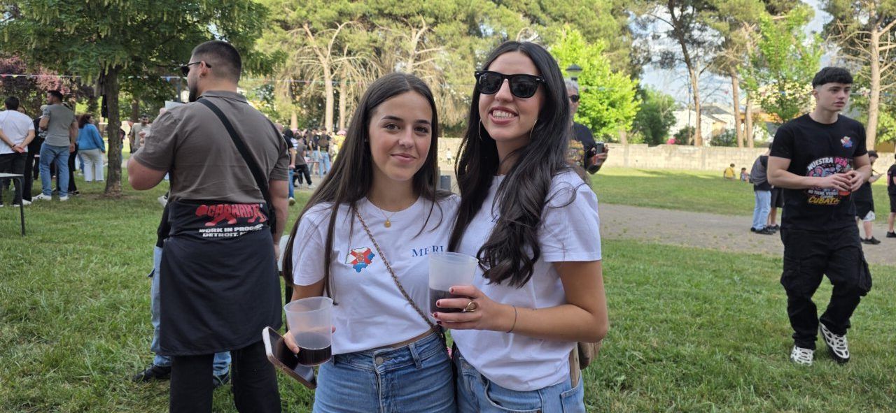 Dos jóvenes sonriendo con vasos en un evento festivo al aire libre