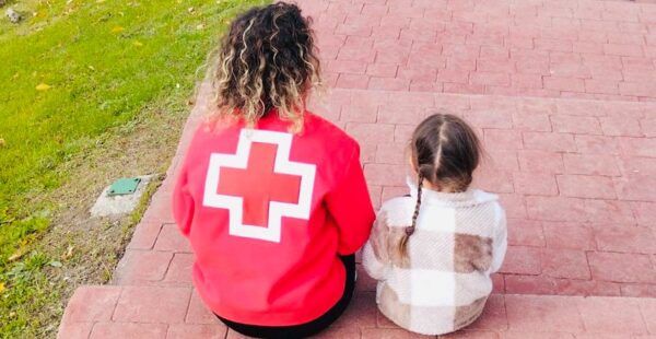 Mujer de Cruz Roja sentada con una niña en un parque