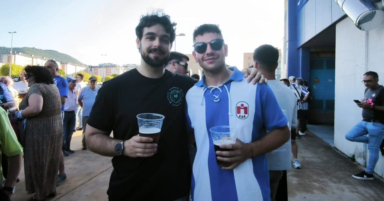 Dos jóvenes sosteniendo cervezas en un bar con gente de fondo