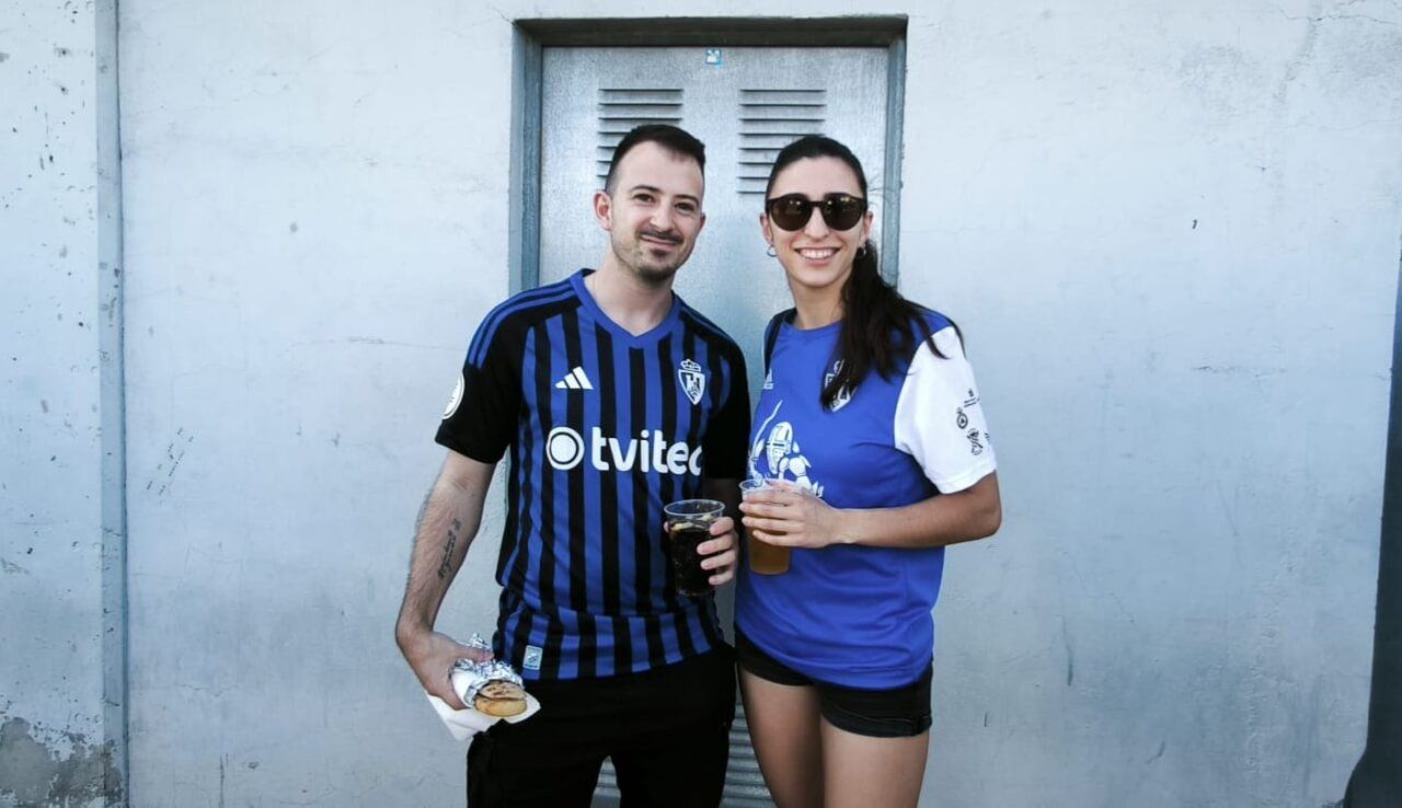 Pareja disfrutando de una bebida en un bar con camisetas de fútbol