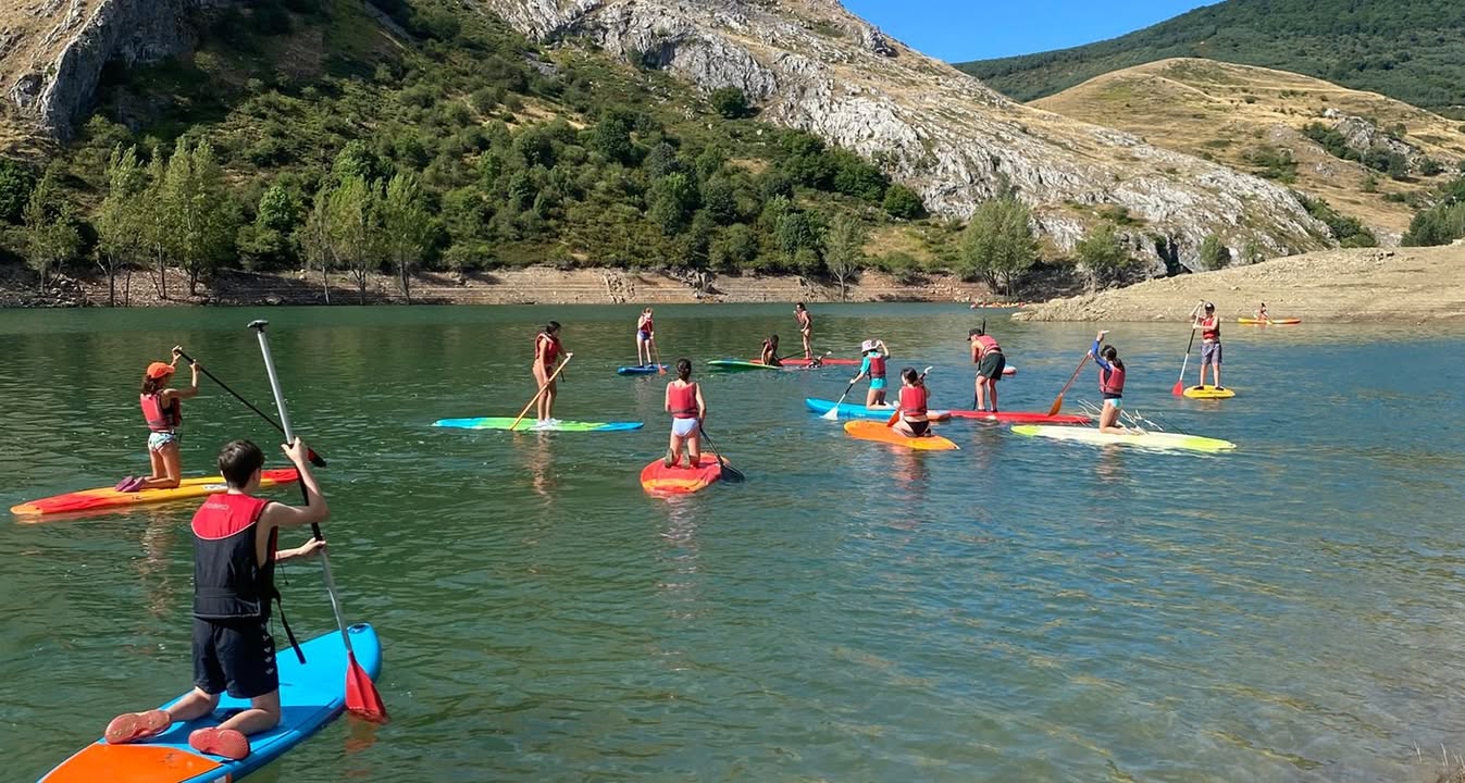 Jóvenes en campamento de verano practicando paddle surf en un lago