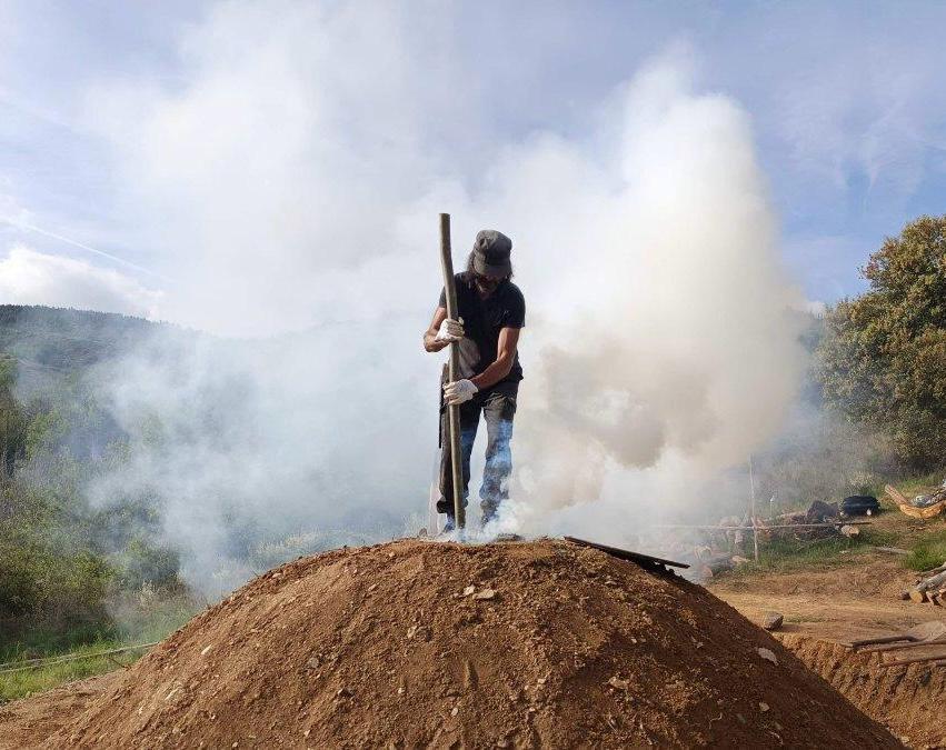 Estudiante trabajando en una carbonera tradicional en un entorno forestal
